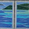 Image showing two mosaics side by side made of hand-made Ceramic Tortuga Tile. Each features a white and grey heron standing in blue and turquoise water with a green island behind them and a blue sky. Each has a grey border around the edge, made of bull nose tile. Each mosaic is 30" square.